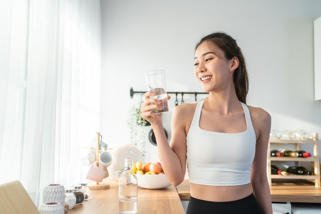Spor kıyafetli Asyalı güzel kadın evde egzersiz yaptıktan sonra su içiyor.