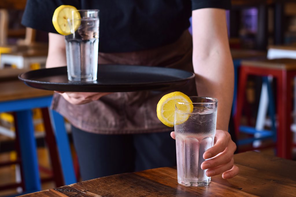 En restauranttjener setter et glass kaldt vann med sitron på bordet.