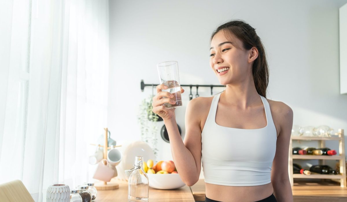 Bella donna asiatica in abbigliamento sportivo beve acqua dopo l'esercizio fisico a casa.