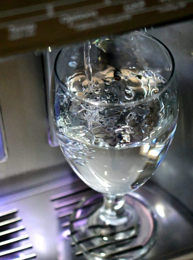 Naplnění skleněného poháru ve dveřním dávkovači vody v chladničce